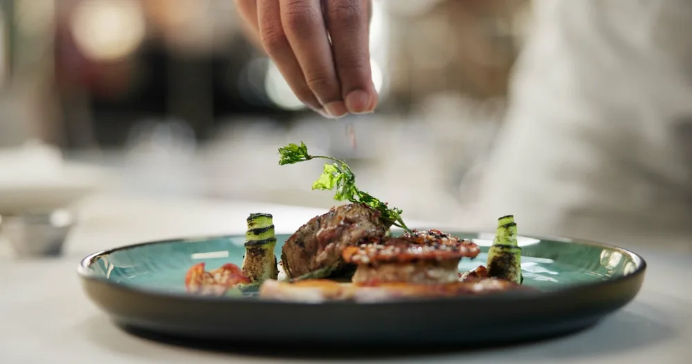 hands sprinkling fine dining food on a culinary dish