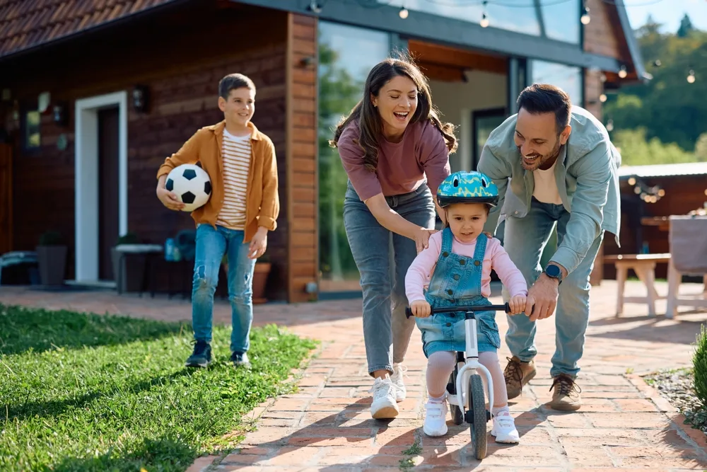 little girl learning to ride a bicycle with help from her parent