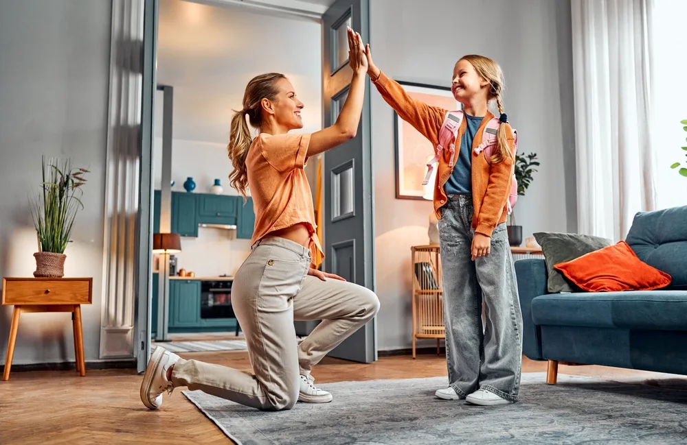 little girl with backpack giving high five to mum standing