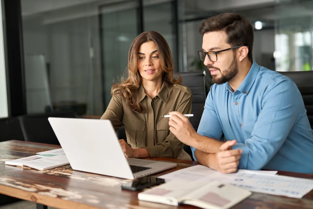 two busy colleagues talking and working together on a laptop in the office