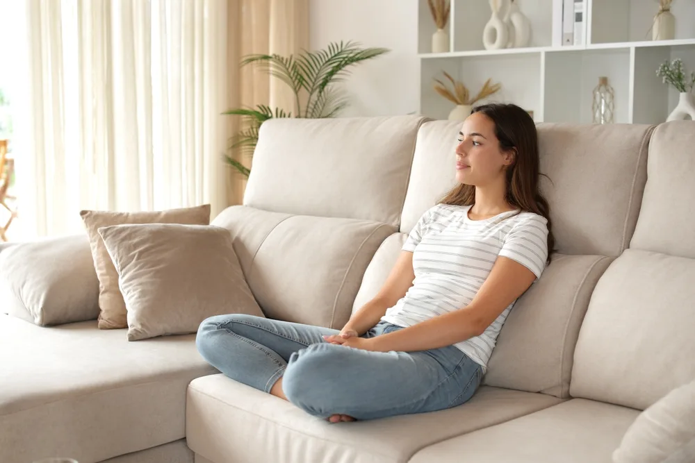 woman on couch contemplating through a window at home wellness