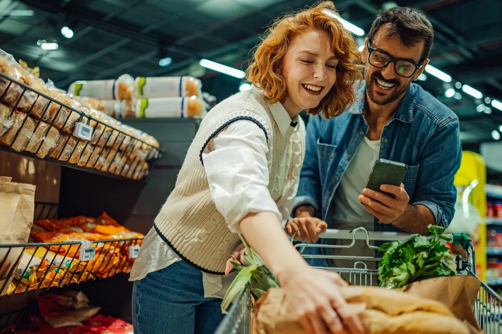 young couple shopping for groceries together using a smartphone in the supermarket